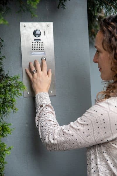Photograph of a woman in a shirt using a video intercom system to enter a building