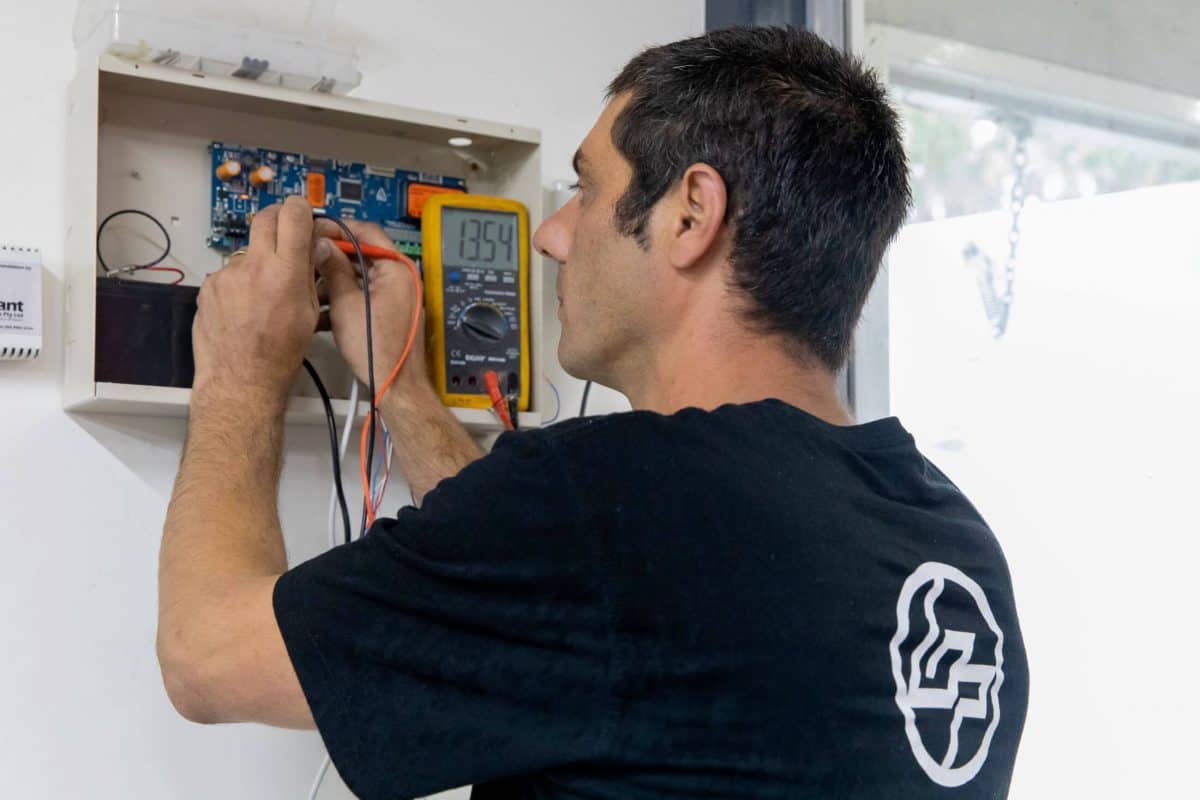 Bpoint technician testing a security panel with a multimeter